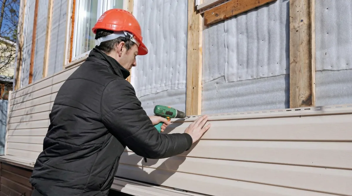 Siding replacement professional using a power drill to install new tan vinyl siding on a home exterior in Birmingham, AL